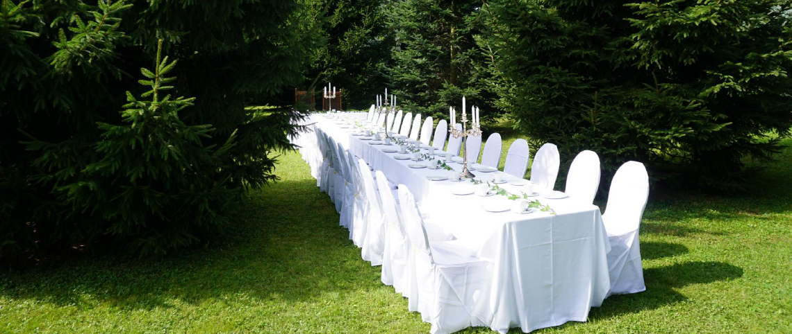 Lange, festlich eingedeckte Tafel im Park der Hochzeitskapelle Callenberg vor dem Tannenwald